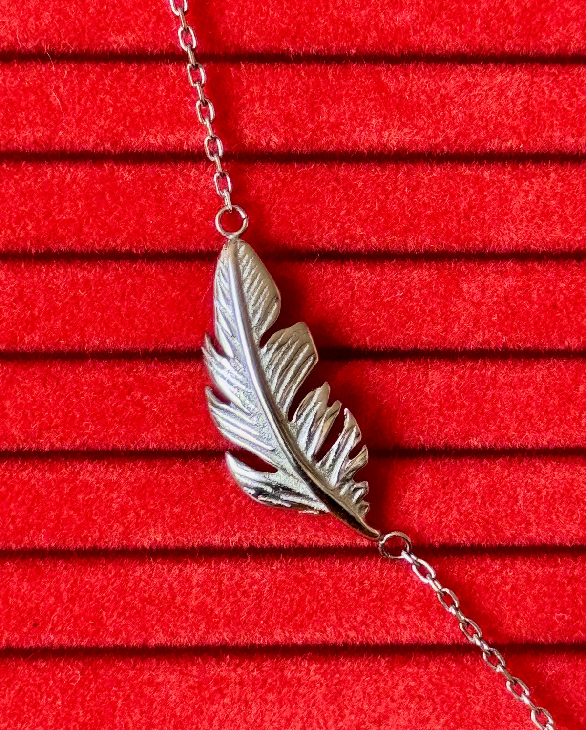 A silver-toned leaf pendant necklace displayed on a textured red velvet background.